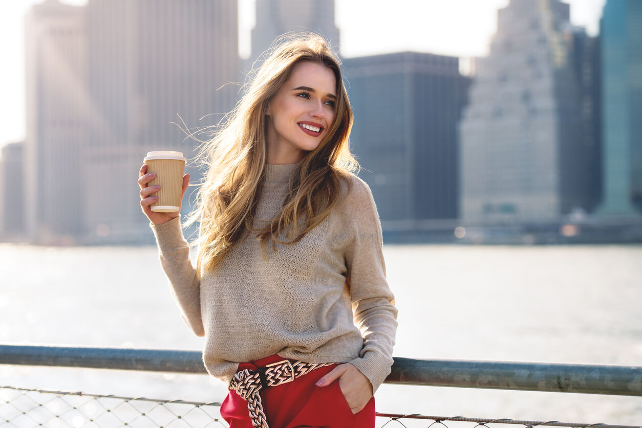 Beautiful woman holding paper coffee cup and enjoying the walk in the city