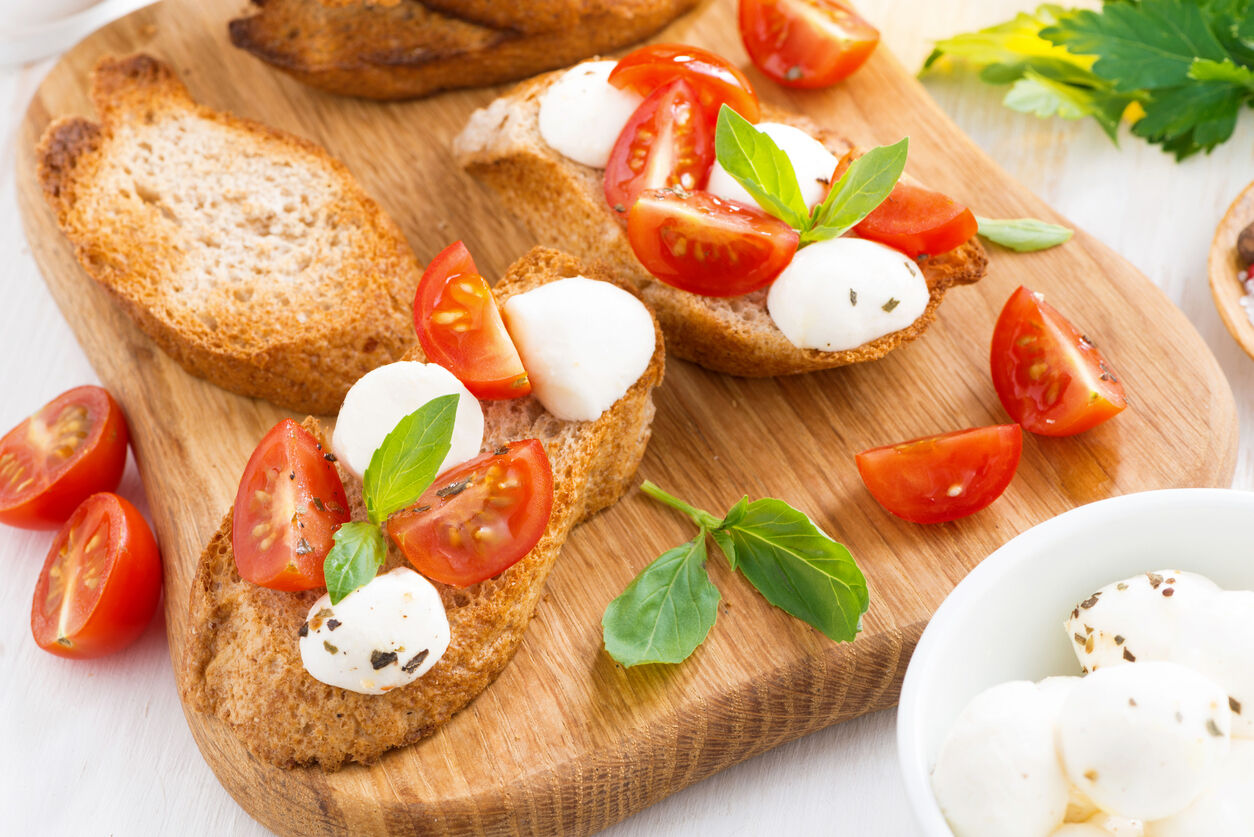 bruschetta with mozzarella, basil and cherry tomatoes on a wooden board, top view, horizontal