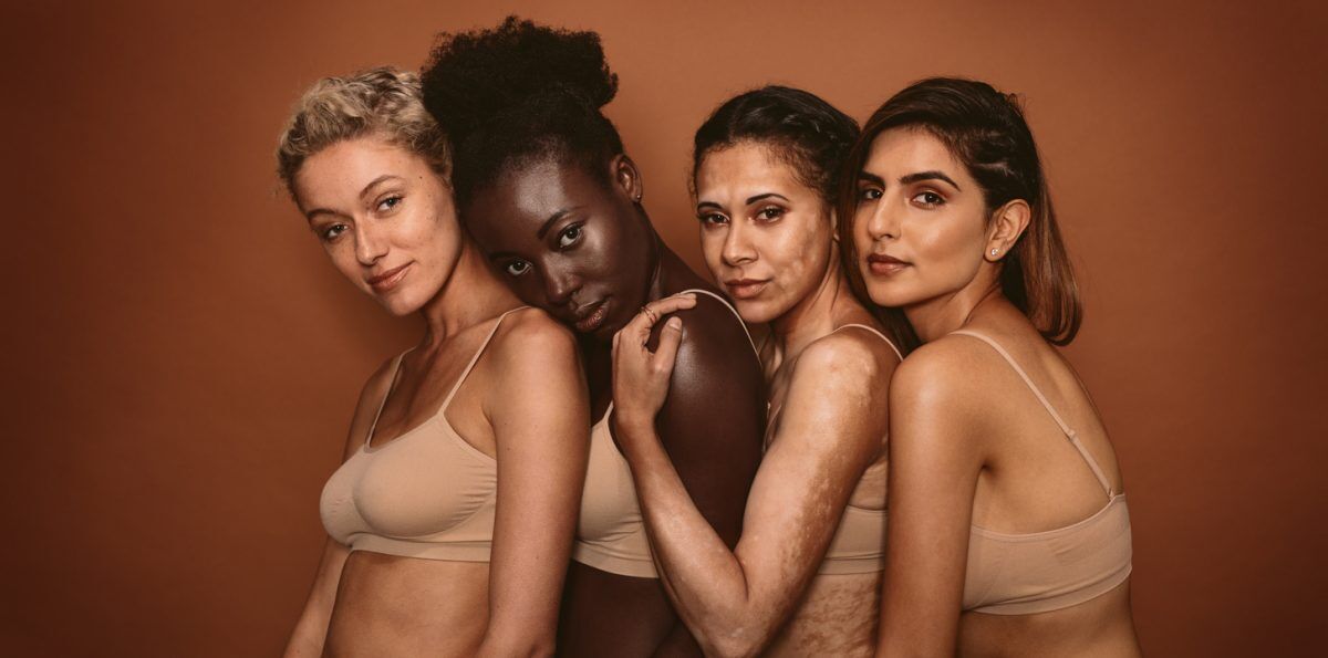 Group of beautiful young women standing together on brown background. Multi ethnic female friends in studio looking at camera.