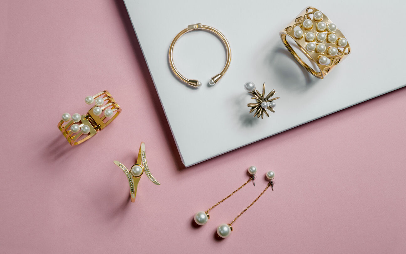 golden bracelets and earrings on pink and white background