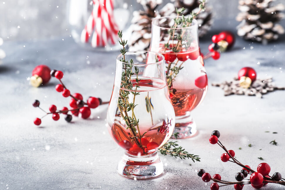 Winter alcoholic cocktail with red berries, liquor, gin, thyme and vodka for Christmas or New Year. Holiday table setting