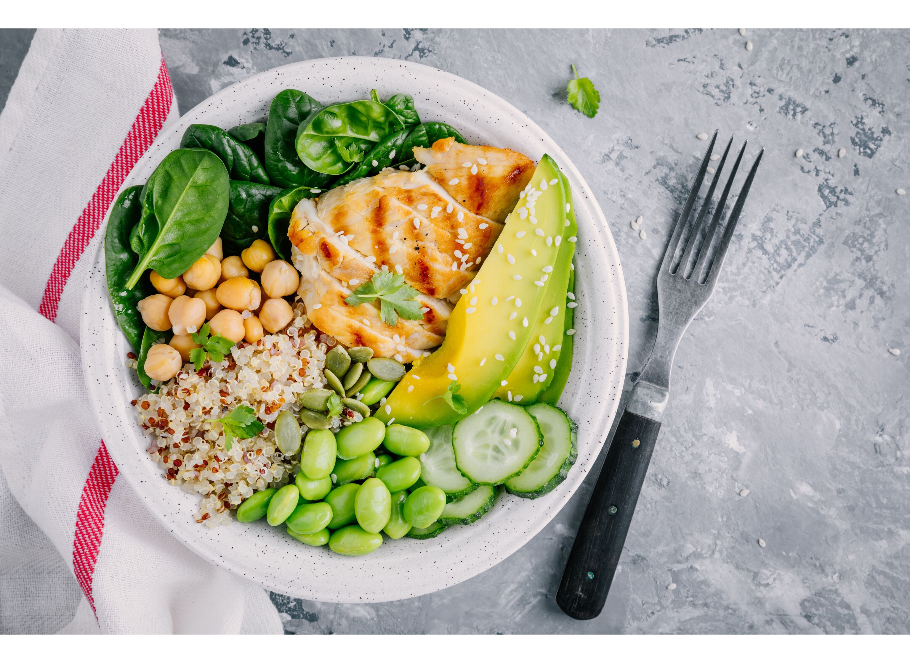 Buddha bowl salad with spinach, quinoa, roasted chickpeas, grilled chicken, avocado, edamame beans, cucumbers, sesame and pumpkin seeds.