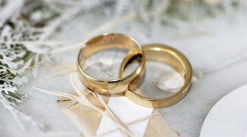 Twee gouden trouwringen op tafel met bloemen en takjes.