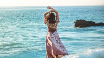 Vrouw op het strand met haar armen omhoog van achter.