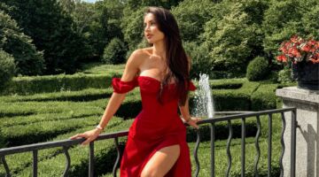 Vrouw in rode jurk voor een tuin.