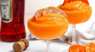 Frozen Mango Aperol cocktail in een glas met een fles Aperol op de achtergrond.