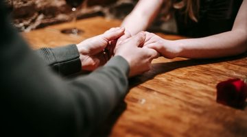 Man en vrouw houden handen vast op tafel.