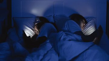 Man en vrouw in bed met telefoon.