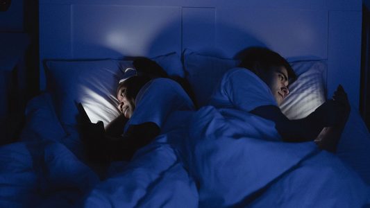 Man en vrouw in bed met telefoon.