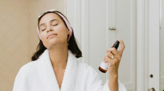 Vrouw spuit haar gezicht in met skincare product.