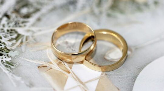 Twee gouden trouwringen op tafel met bloemen en takjes.