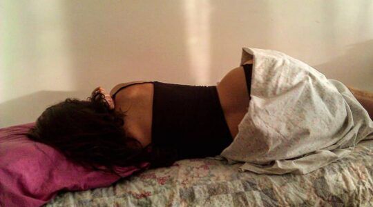 Vrouw slaapt op haar zijde op een bed richting de muur