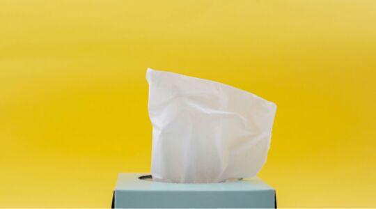 Blauwe tissuedoos met een tissue eruit voor een gele achtergrond.