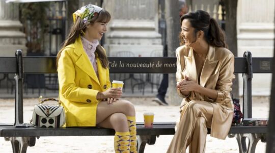 Emily in Paris met Mindy koffie aan het drinken op een bankje.