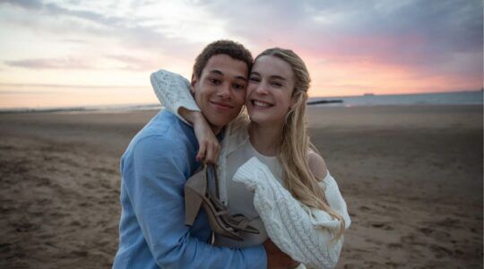 Personages van Knokke Off omhelzen elkaar op het strand.