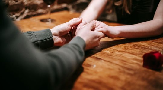 Man en vrouw houden handen vast op tafel.