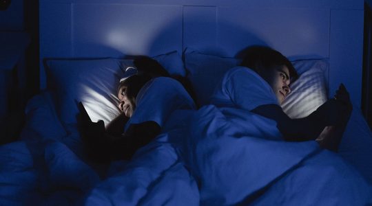 Man en vrouw in bed met telefoon.