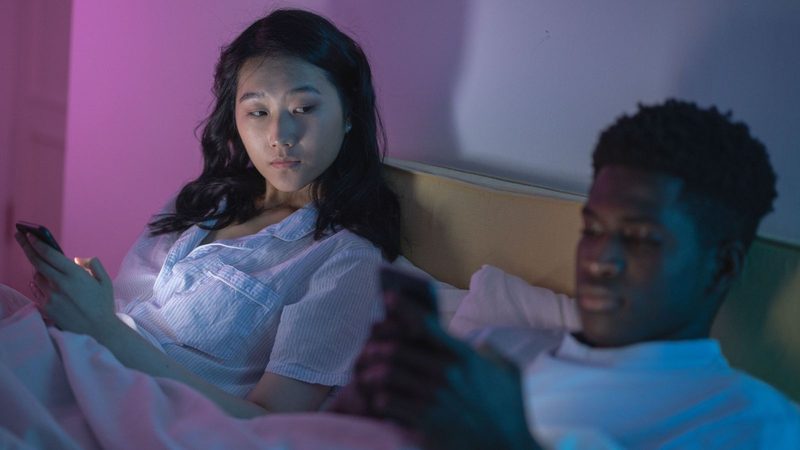 Vrouw en man in bed met telefoons vast.