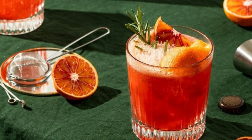 Een cocktail glas op tafel met fruit eromheen.