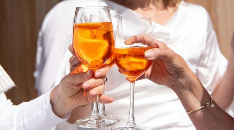 Vrouwen met een oranje cocktail in de handen proosten.